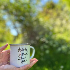 The Plum Village Enamel Mug, adorned with Thich Nhat Hanh’s “Drink your tea” calligraphy, glows in soft light