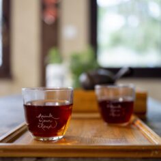 A serene table setting featuring the Plum Village Tea Glass engraved with “Drink your clouds” by Thich Nhat Hanh, surrounded by a teapot and blooming flowers