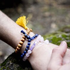 Plum Village wrist mala collection featuring different materials: light wood, jasper, lapis lazuli, and rose quartz, displayed on a natural surface.