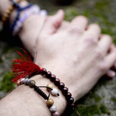 Plum Village wrist mala collection featuring different materials: light wood, jasper, lapis lazuli, and rose quartz, displayed on a natural surface