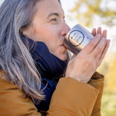 A practitioner holding the Plum Village Insulated Stainless Steel Water Bottle for a mindful hydration, with a bright sky in the background; Gourde isotherme en acier inoxydable Plum Village pour l'hydratation en pleine conscience