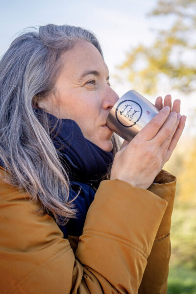 A practitioner holding the Plum Village Insulated Stainless Steel Water Bottle for a mindful hydration, with a bright sky in the background; Gourde isotherme en acier inoxydable Plum Village pour l'hydratation en pleine conscience