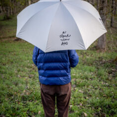 Practitioner walking peacefully under Plum Village Calligraphy Umbrella showing A Cloud Never Dies zen calligraphy on sunny path; arapluie Calligraphie Plum Village sous la pluie pour marcher en pleine conscience